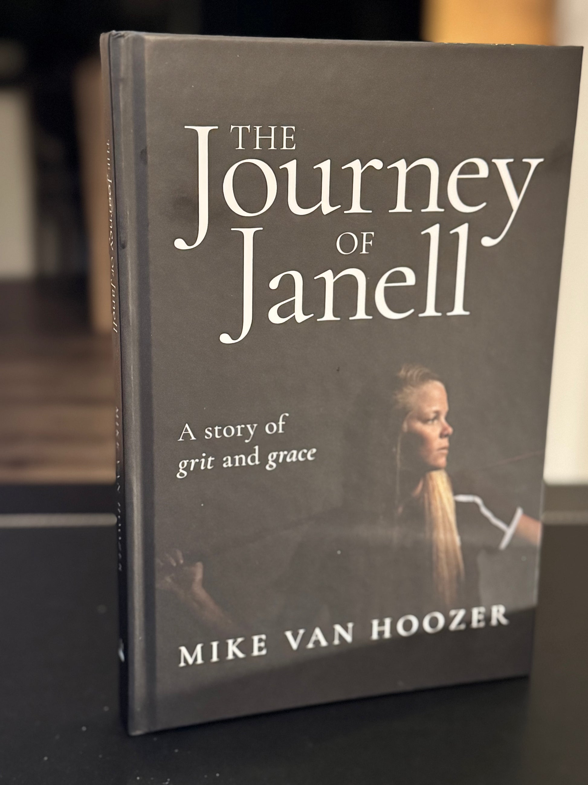 Book titled 'The Journey of Janell' by Mike Van Hoozer on a dark surface in an office